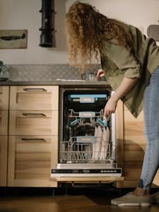 A woman loads dishes into a modern automatic dishwasher in a stylish kitchen setting.