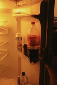 An open fridge filled with various beverages including Coca-Cola under warm lighting.